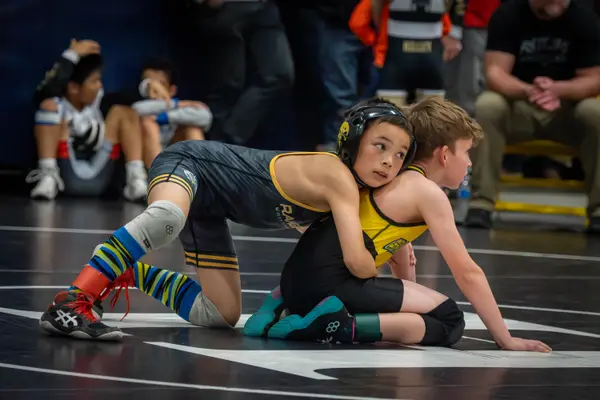 A young Rangers wrestler holds an opponent from behind and looks toward the camera