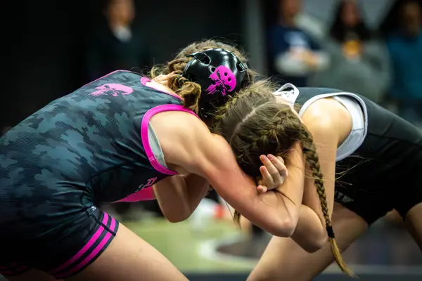 Two wrestlers lock heads in a tie-up, one in a pink Rangers singlet