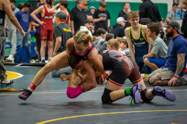 A Rangers wrestler in pink drives an opponent toward the mat as spectators watch