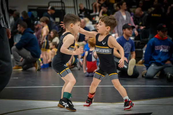 Two young wrestlers in Rangers singlets grapple on a black mat