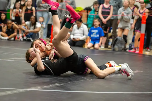 Two wrestlers scramble on the mat as spectators watch from the rope