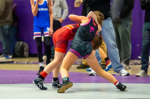 A Rangers wrestler ties up with an opponent in red on a purple mat