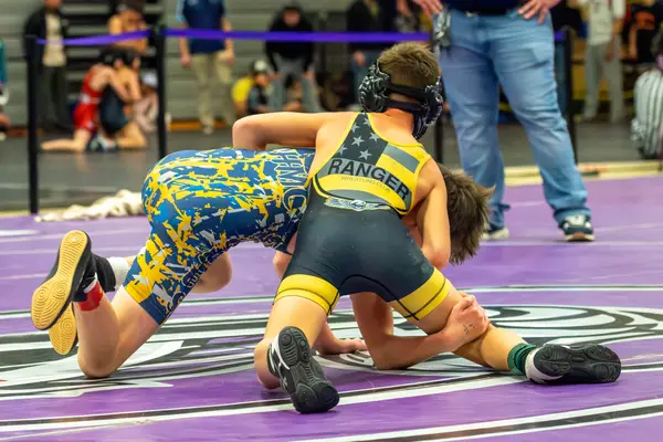 A Rangers wrestler rides an opponent in a camo singlet on a purple mat