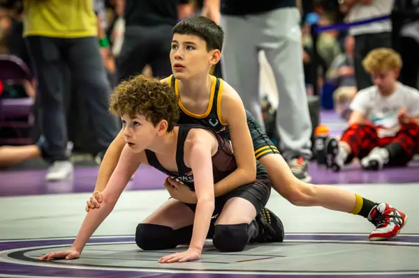 A Rangers wrestler rides an opponent as both look toward the mat edge