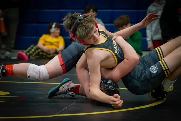 A Rangers wrestler in pink headgear works to turn an opponent on a black mat