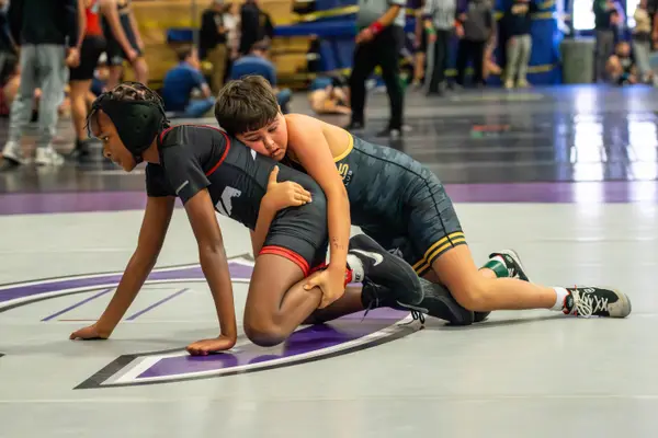 A Rangers wrestler rides an opponent on a gray and purple mat