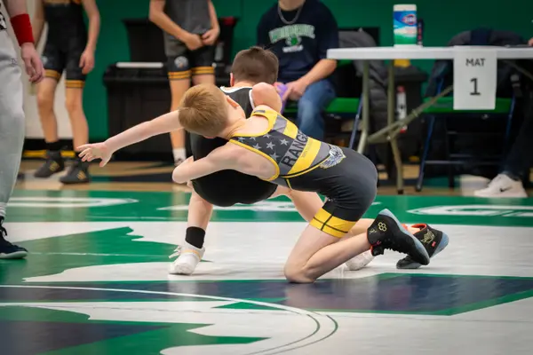 A young Rangers wrestler drives an opponent backward on a green mat