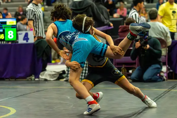 A Rangers wrestler lifts an opponent's leg on a black mat