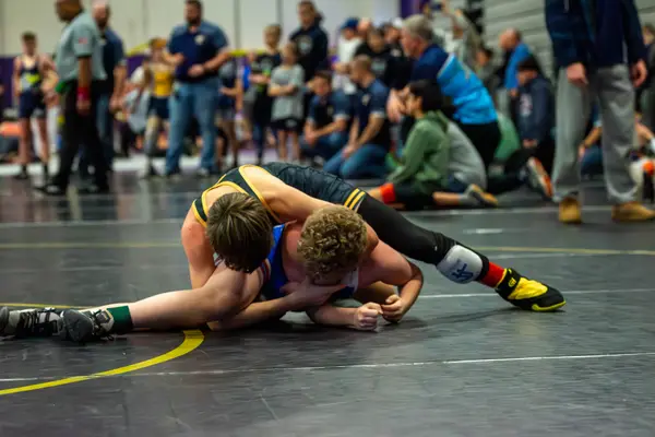 A Rangers wrestler works on top of an opponent on a dark mat