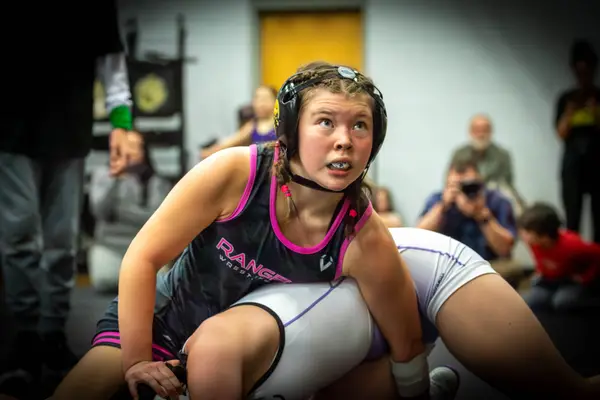 A Rangers wrestler in pink-trimmed gear looks up while riding an opponent