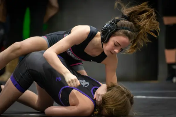 Two wrestlers on a dark mat, one riding the other