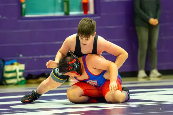A wrestler controls an opponent in a red and blue singlet