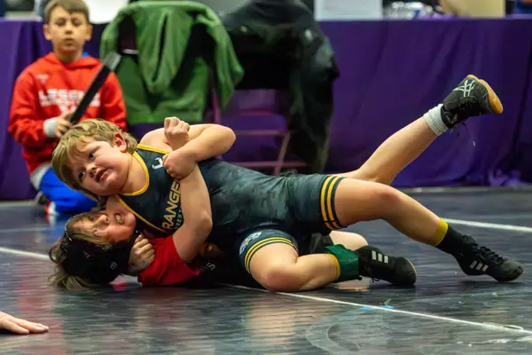 A young Rangers wrestler holds an opponent in a cradle and looks toward the camera