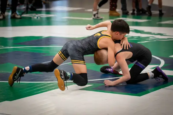 A Rangers wrestler shoots in on an opponent on a green and white mat