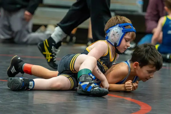 A young Rangers wrestler in blue headgear works on top of an opponent