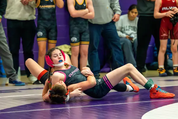 A Rangers wrestler in pink headgear holds an opponent down on a purple mat