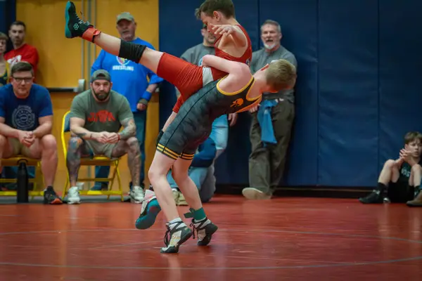 A Rangers wrestler lifts an opponent off the mat as fans watch from the wall