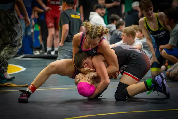 A Rangers wrestler rides an opponent as spectators watch from the mat edge