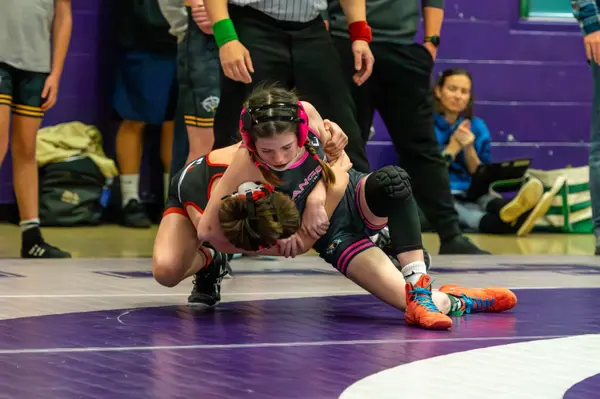 A Rangers wrestler in pink headgear works an opponent on a purple mat
