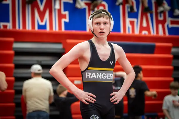 A Rangers wrestler stands with hands on hips beside the bleachers during a tournament
