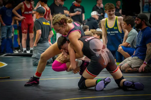 A Rangers wrestler in pink drives into an opponent as spectators watch