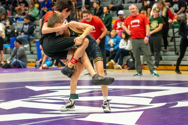 A young wrestler lifts an opponent off the mat in front of a crowd