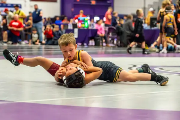 A young Rangers wrestler works for a pin on a gray and purple mat