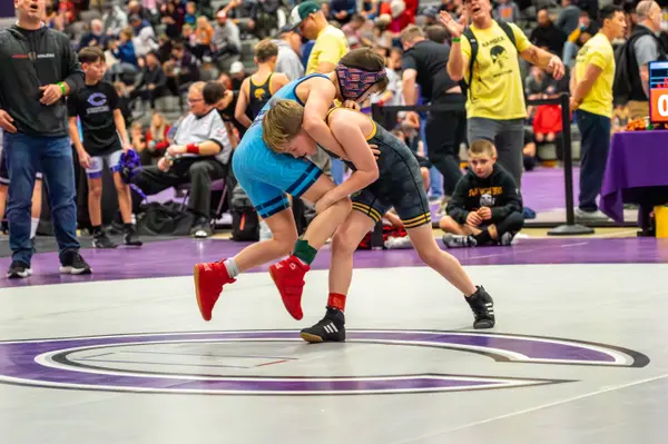 A Rangers wrestler lifts an opponent in light blue on a purple mat