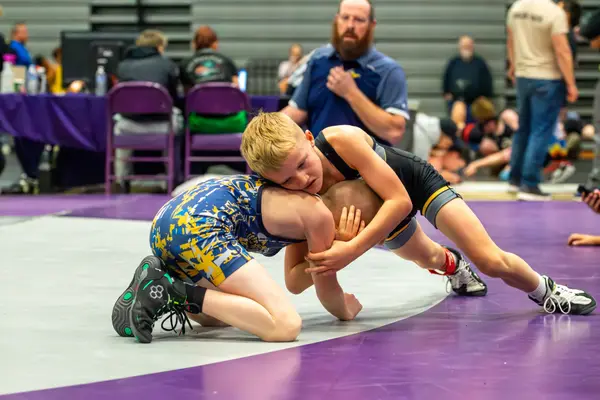 A Rangers wrestler wraps up an opponent in a camo singlet on a purple mat