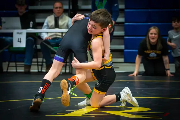A young Rangers wrestler lifts an opponent's leg as spectators cheer from the mat edge