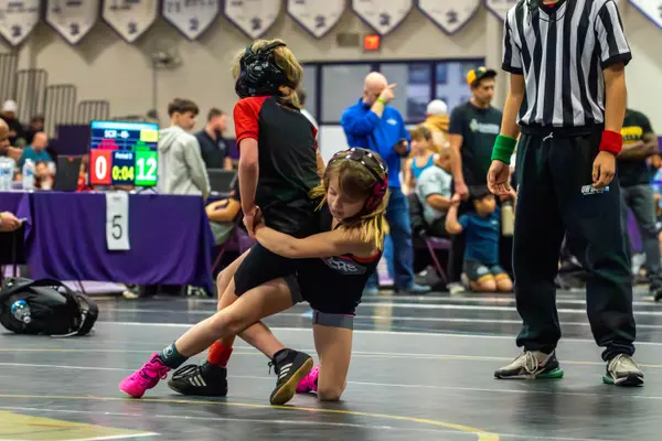 A young wrestler drives an opponent in front of the referee