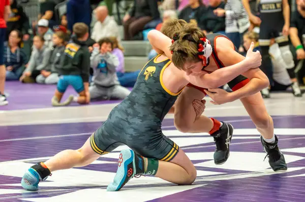 A Rangers wrestler ties up with an opponent in red on a purple mat